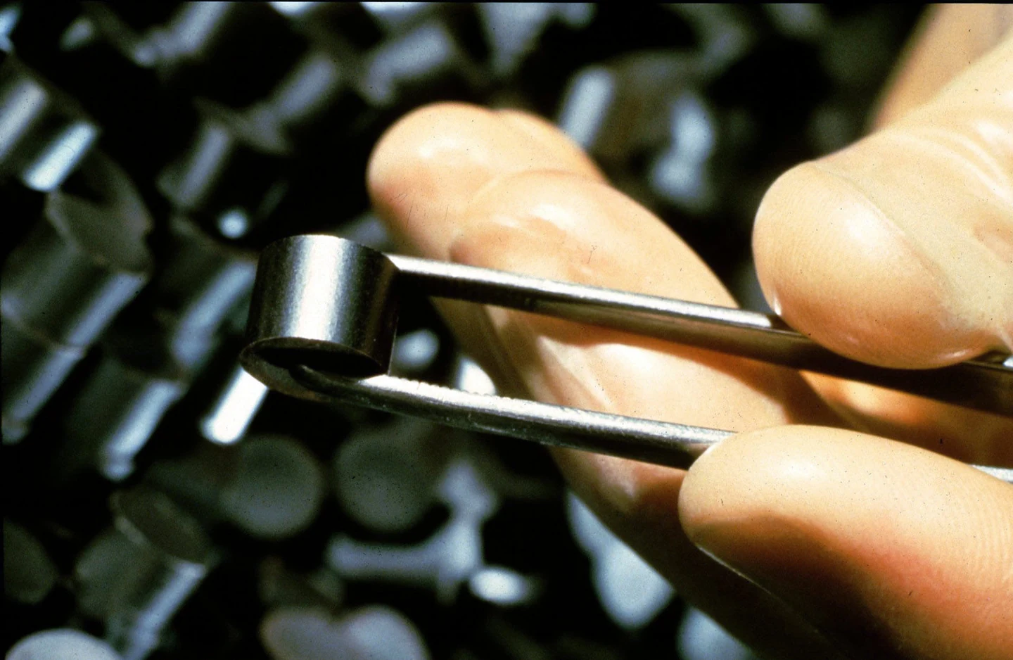 A real fuel pellet held with tweezers beside the operator’s fingers.