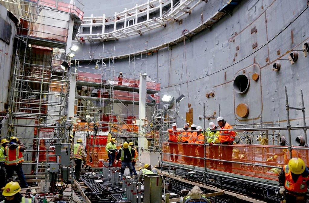 NRC staff visit the inside of Vogtle Unit 3 containment during construction. People stand among equipment and scaffolding inside the large steel structure.